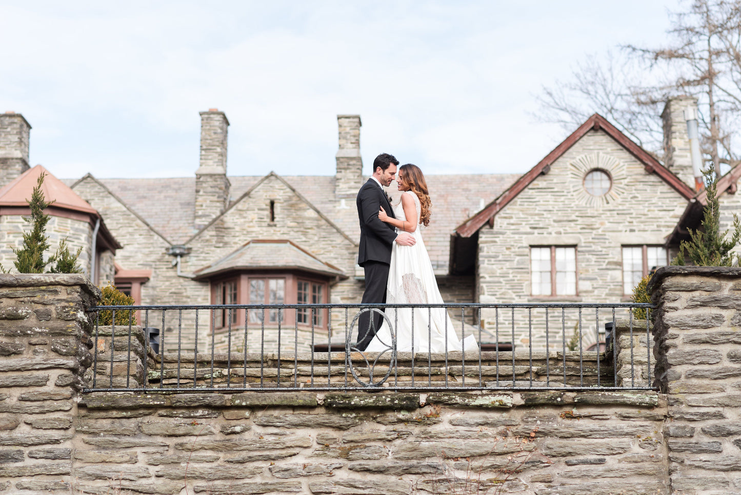 Bride wearing a Priscilla Couture Bound wedding dress with her groom standing on the patio of a mansion.