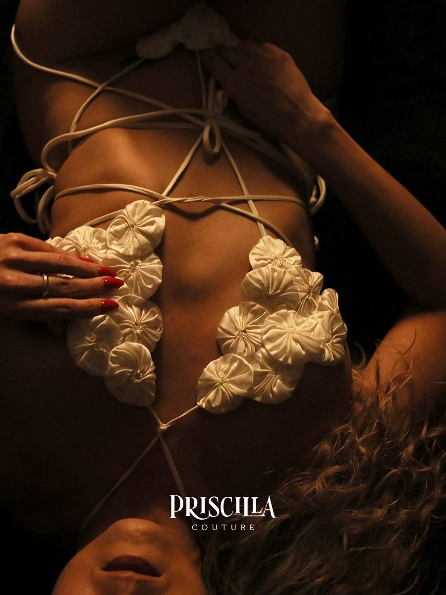 White floral top with lace-up back on a dark background, featuring the brand 'Priscilla Couture'.
