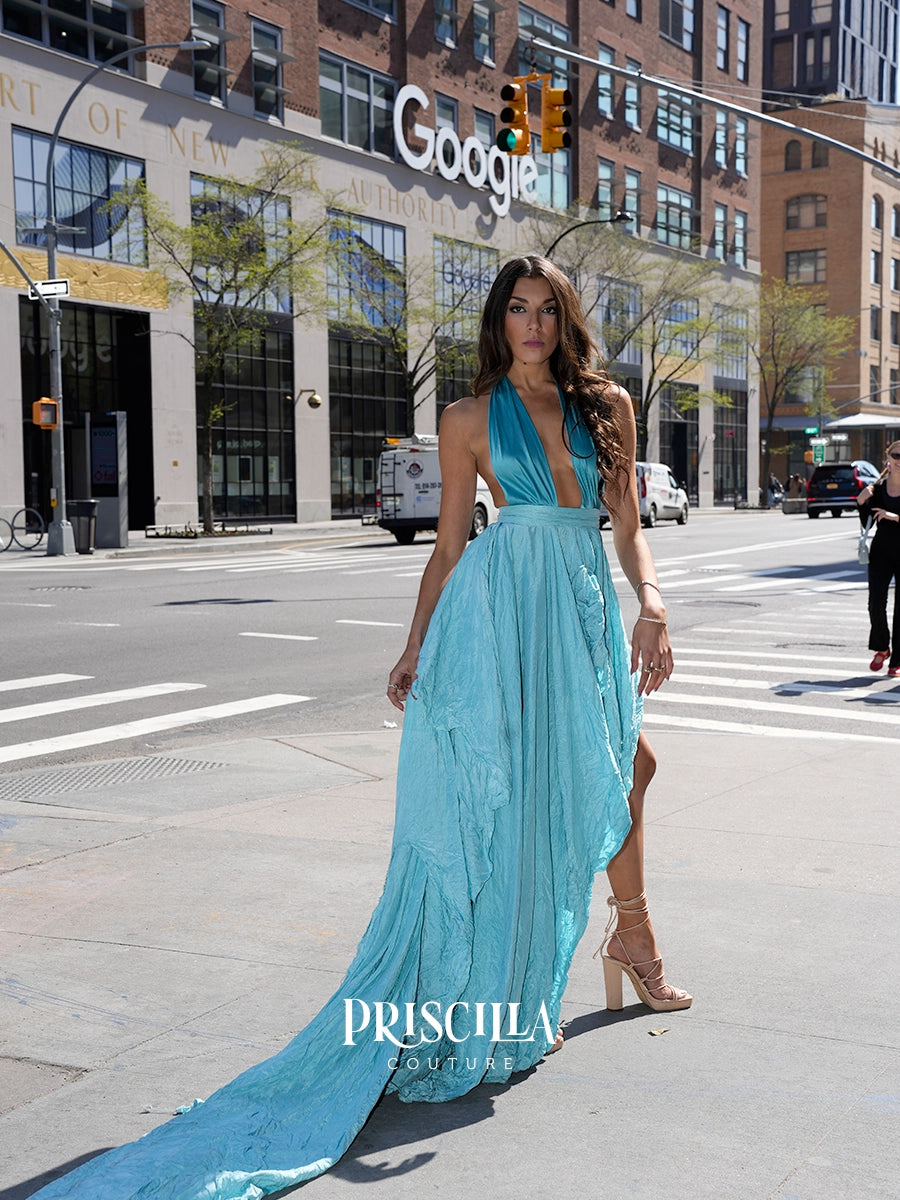 A woman models a light blue halter-neck maxi dress with a deep V-neckline, a flowing skirt, and a long train on a city street. The Google building is visible in the background, and a 'PRISCILLA COUTURE' watermark is at the bottom.