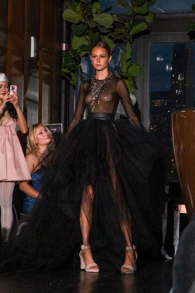 Model wearing a black, sheer dress with a high slit on a runway.