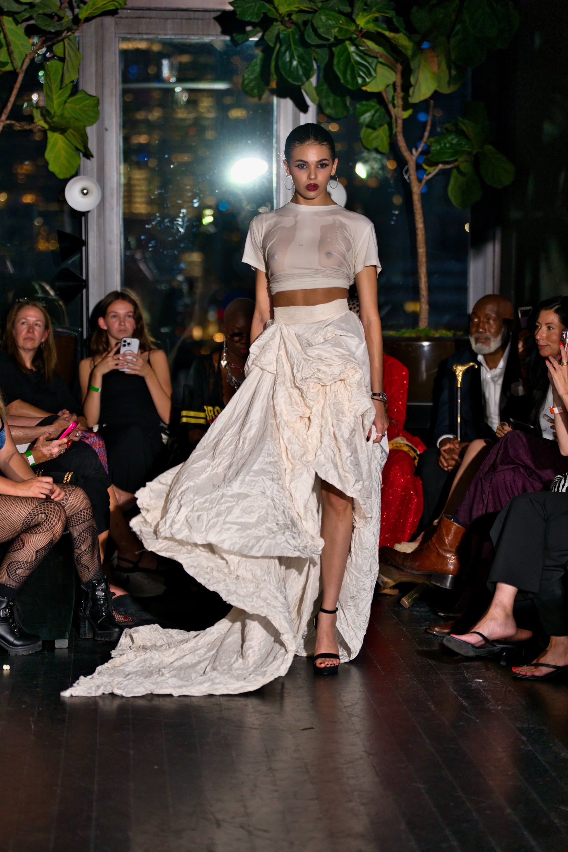 Model walking on a runway wearing a wet F white tee outfit with a rebellious, textured skirt.