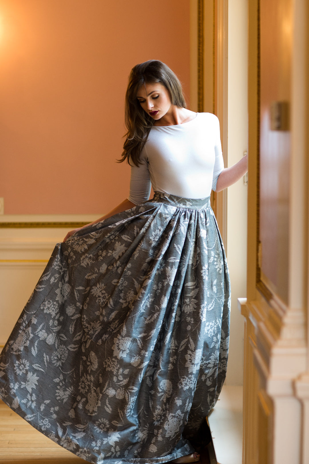 Woman wearing a Priscilla Couture white top and gray floral skirt in an indoor setting