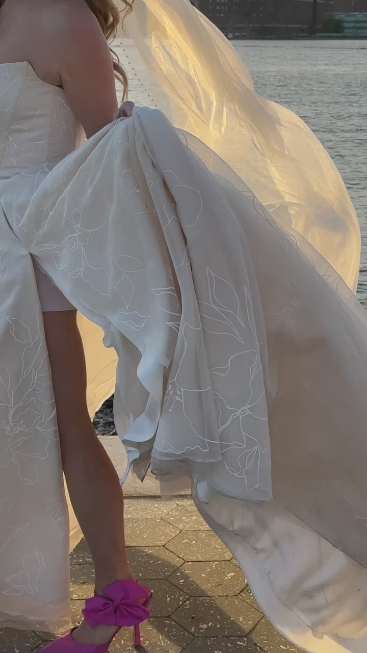 NYC bride in her Priscilla Couture custom wedding gown with her groom walking by the river. NYC skyline clear in the background.