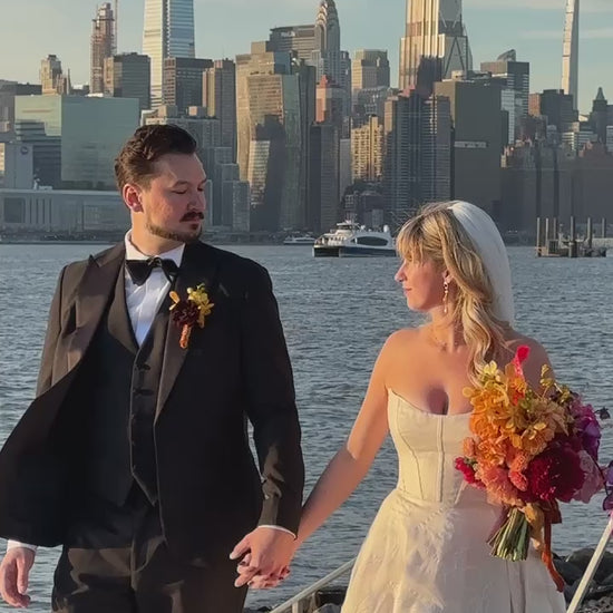 Bride in a Priscilla Couture custom wedding gown with her groom walking by the river. NYC skyline in the background.