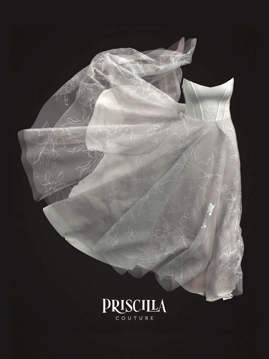 A 3D avatar of a Priscilla Couture custom white sheer tulle dress with delicate floral embroidery, captured in a dramatic floating pose against a solid black background, with the brand name 'PRISCILLA COUTURE' printed at the bottom.