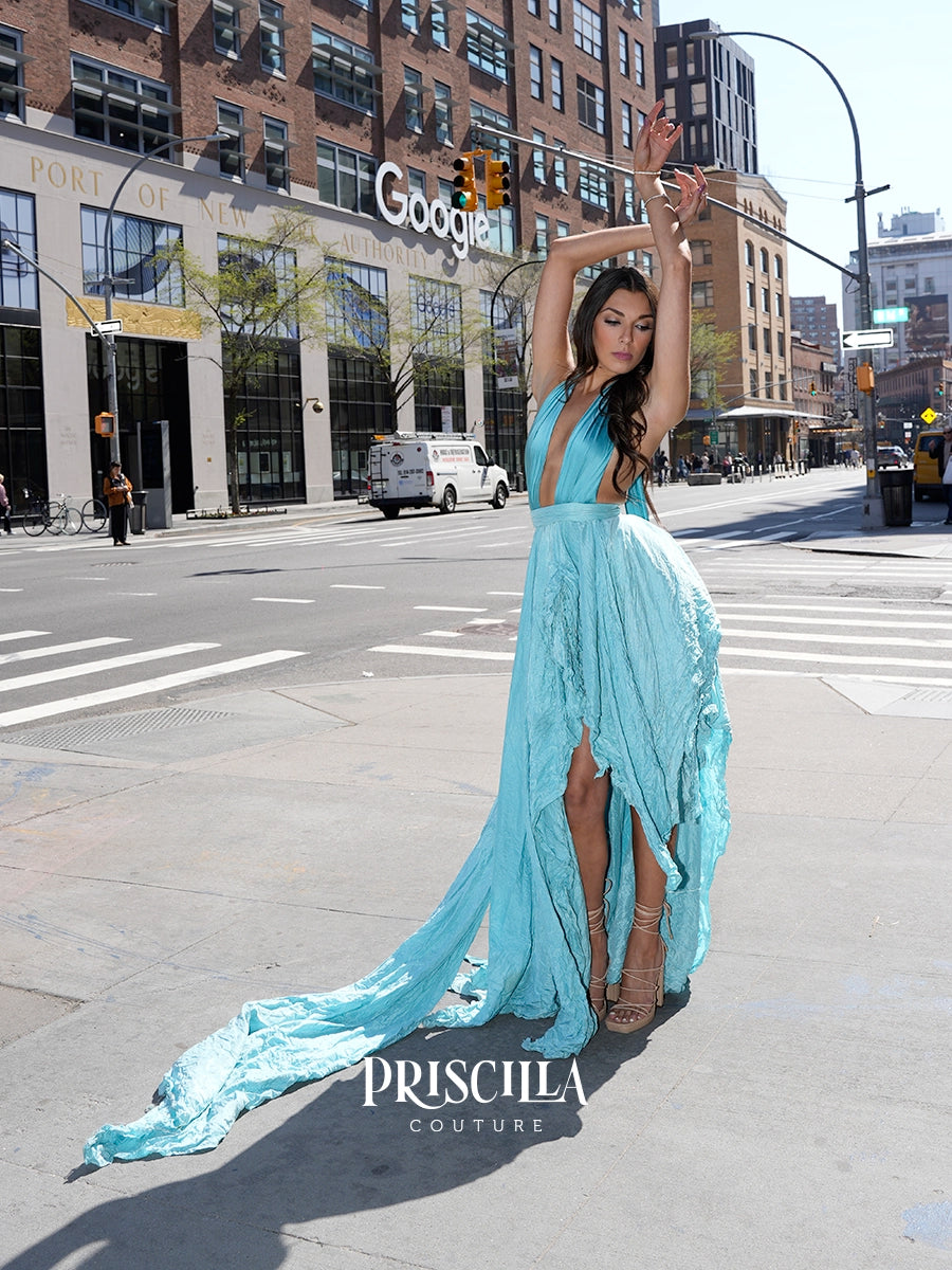 A woman modeling a light blue custom gown with a long flowing train on a NYC street. The Priscilla Couture dress features a deep V-neckline, a high thigh slit, and a dramatic train that spreads across the pavement.