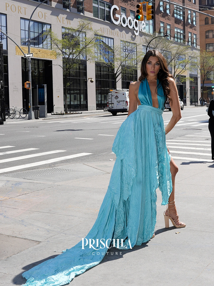 A woman models a light blue halter-neck gown with a deep V-neckline and a long flowing train on a NYC street. The dress features a sheer lace overlay and a solid mesh skirt.