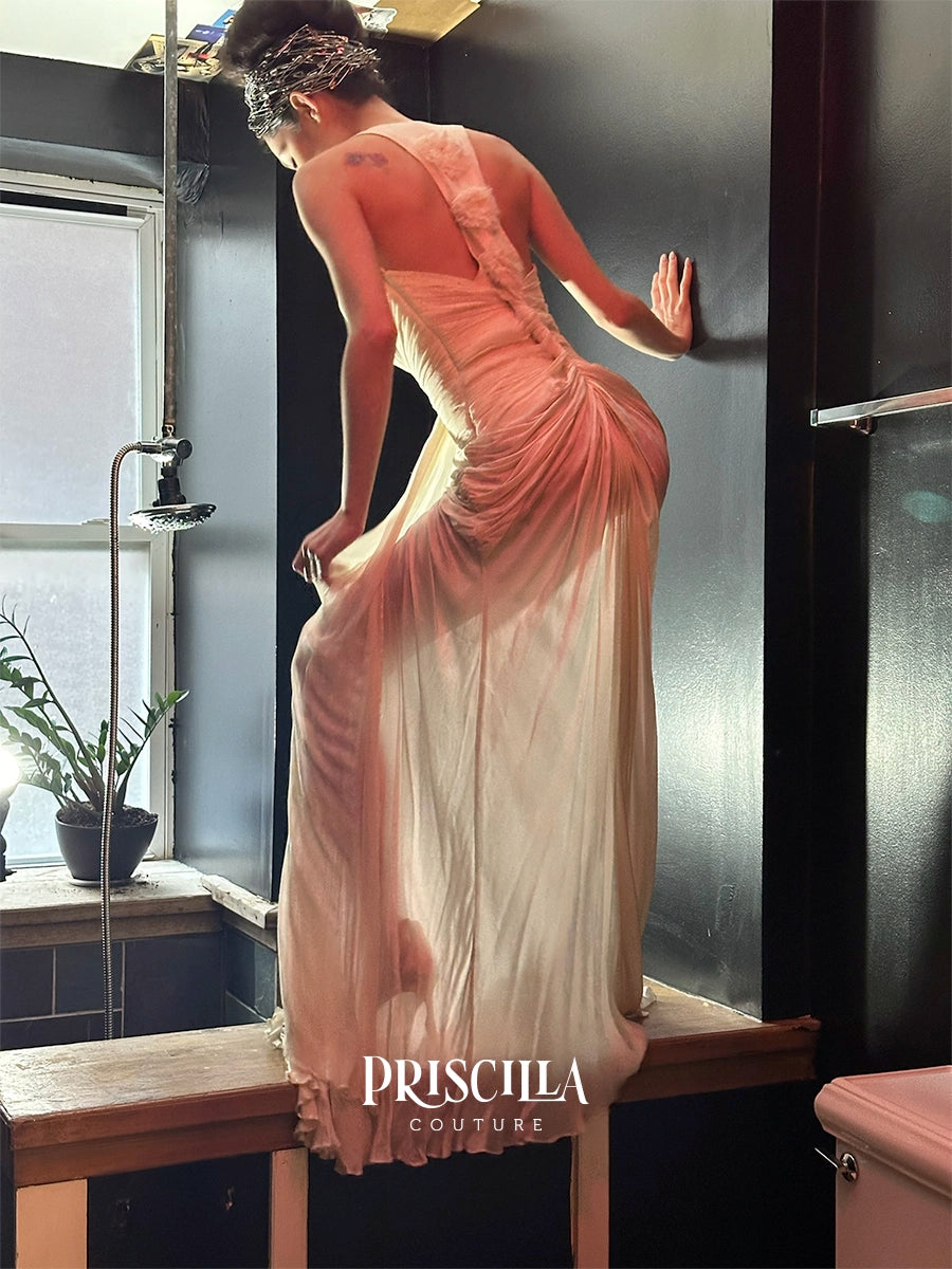 A model wearing a draped Georgette couture wedding dress stands on a wooden bench in a dark bathroom setting, viewed from behind to show the back of the dress. The brand name 'PRISCILLA COUTURE' is displayed at the bottom.