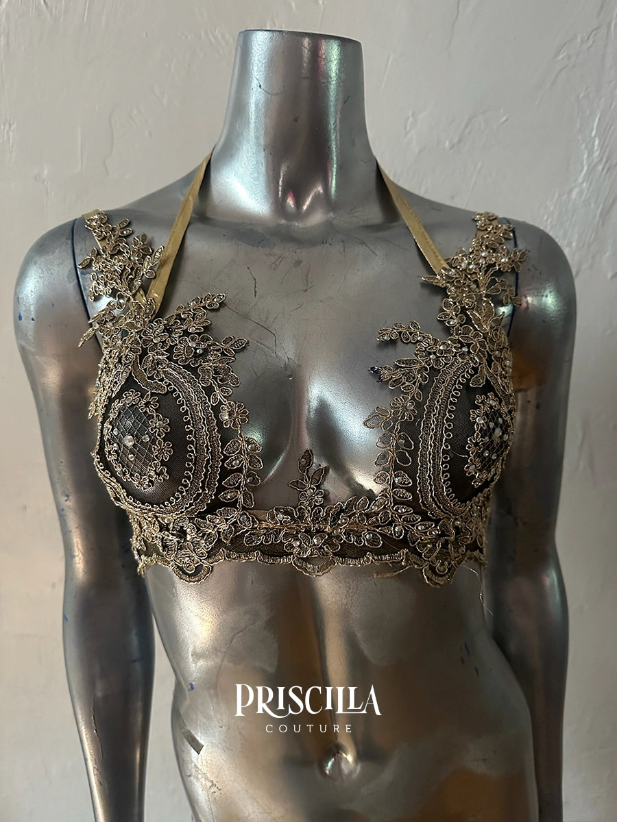 An ornate silver-toned Priscilla Couture halter bralette with intricate lace applique and beadwork, displayed on a metallic mannequin torso. 