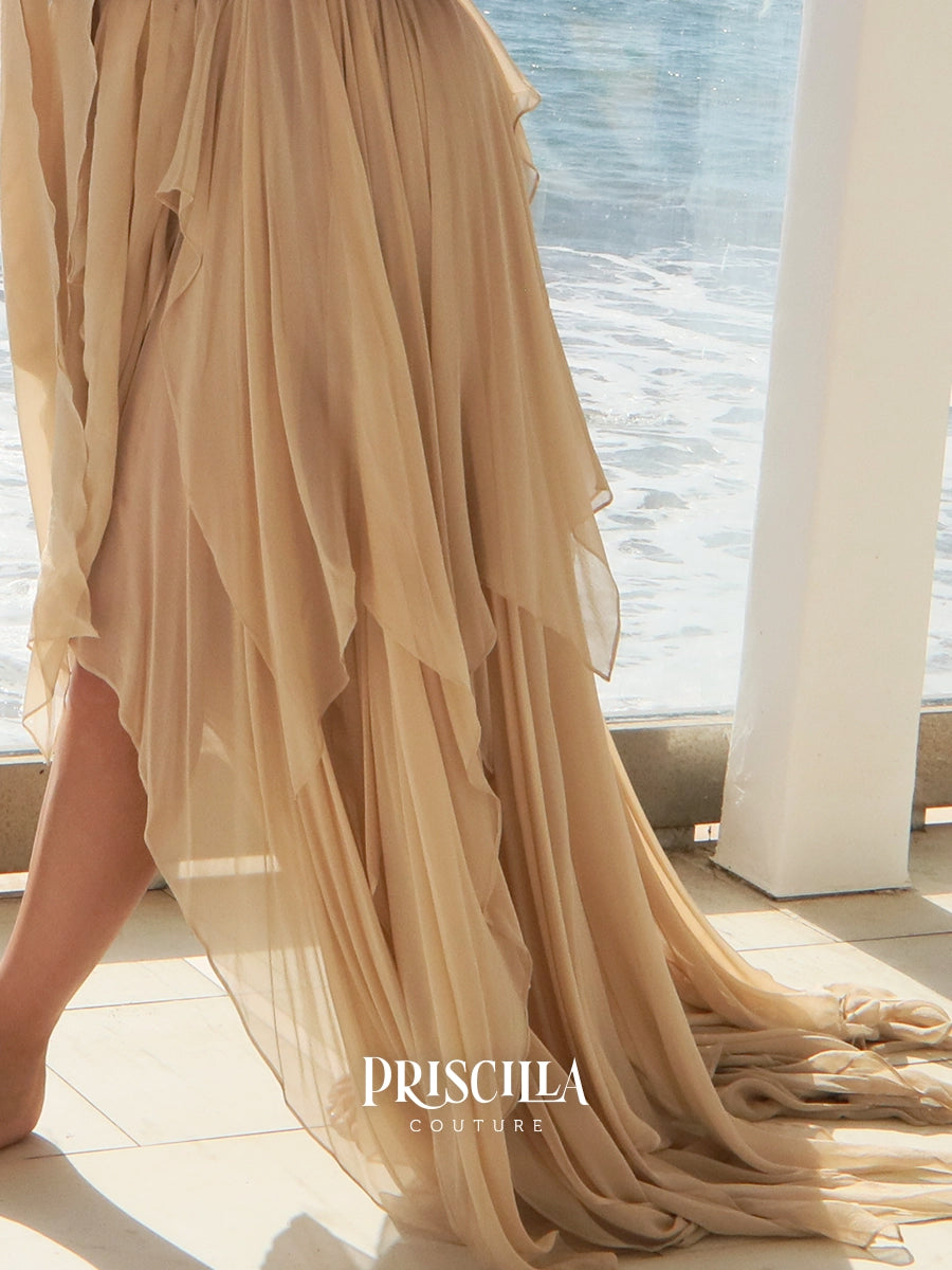 A flowing champagne beige chiffon skirt with layered ruffles and a long train, worn by a model standing on a balcony with the ocean in the background. The brand name 'PRISCILLA COUTURE' is printed on the dress.