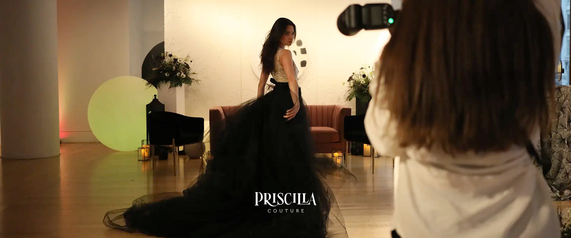 Model in a Priscilla Couture gown being photographed by a professional in a studio setting.