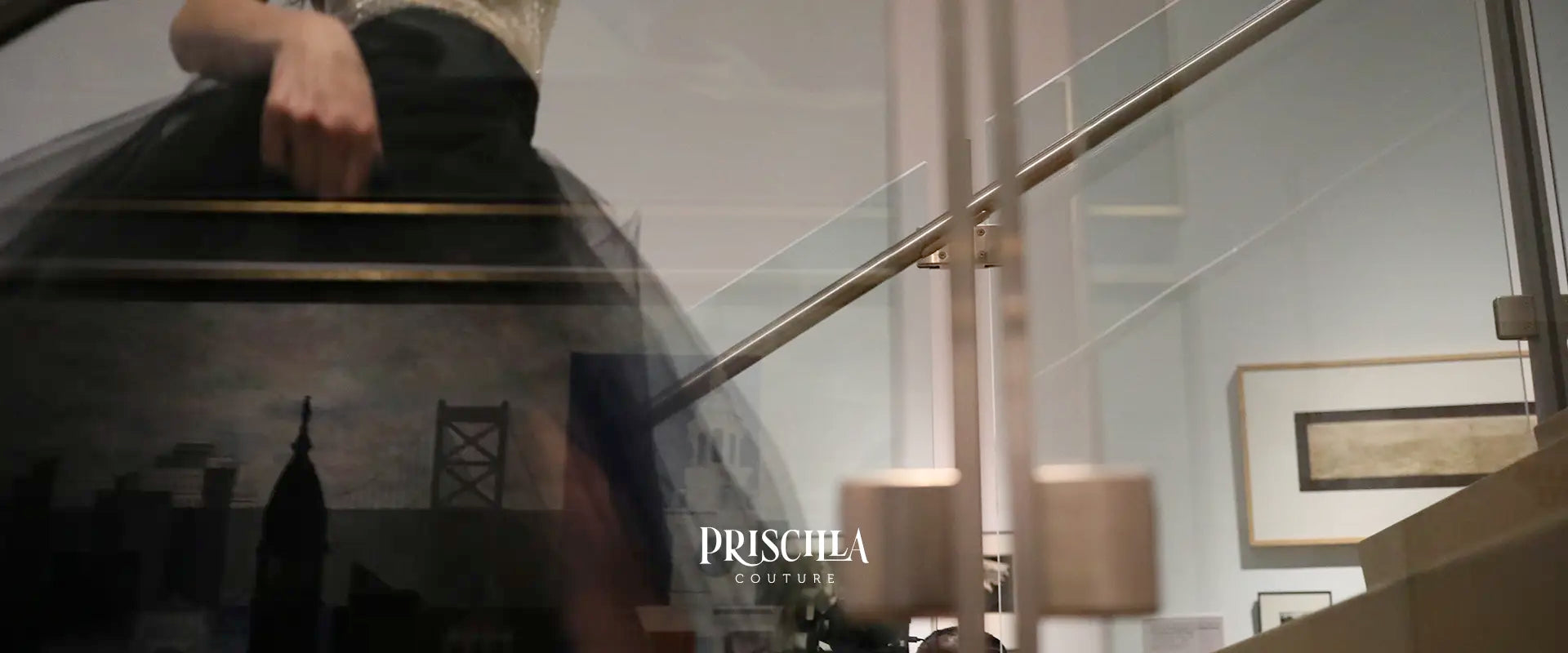 Model walking up a staircase in a Priscilla Couture  black skirt with modern interior setting and 'Priscilla Couture' branding.