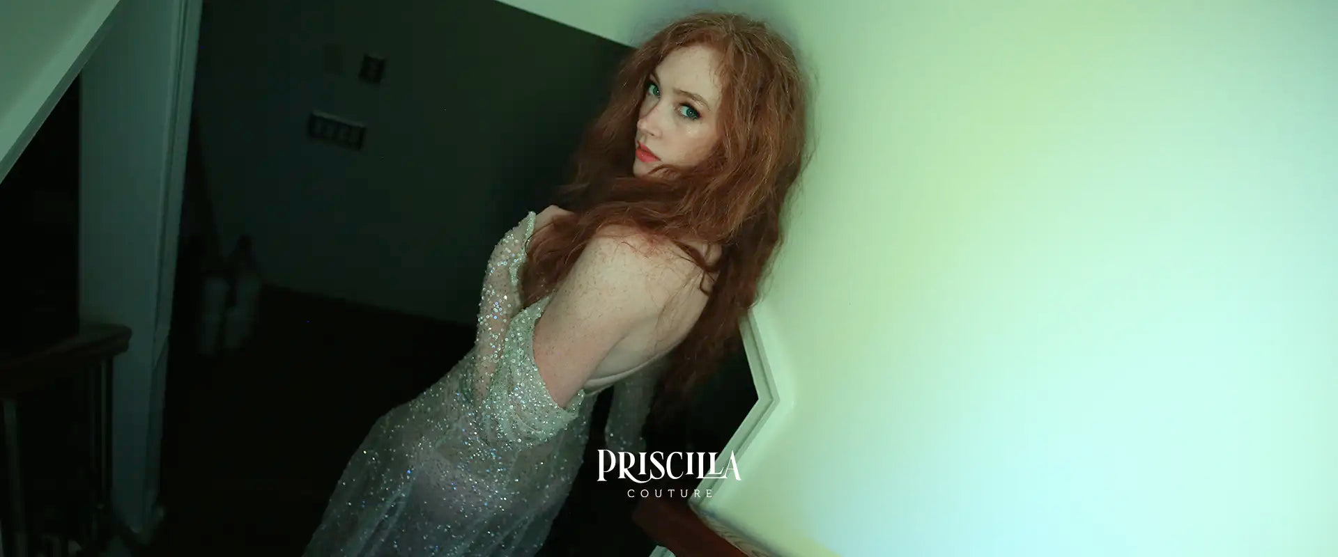 Bride in a sparkly Priscilla Couture's beaded wedding dress with 'Priscilla Couture' logo and branding in a dimly lit stairway.