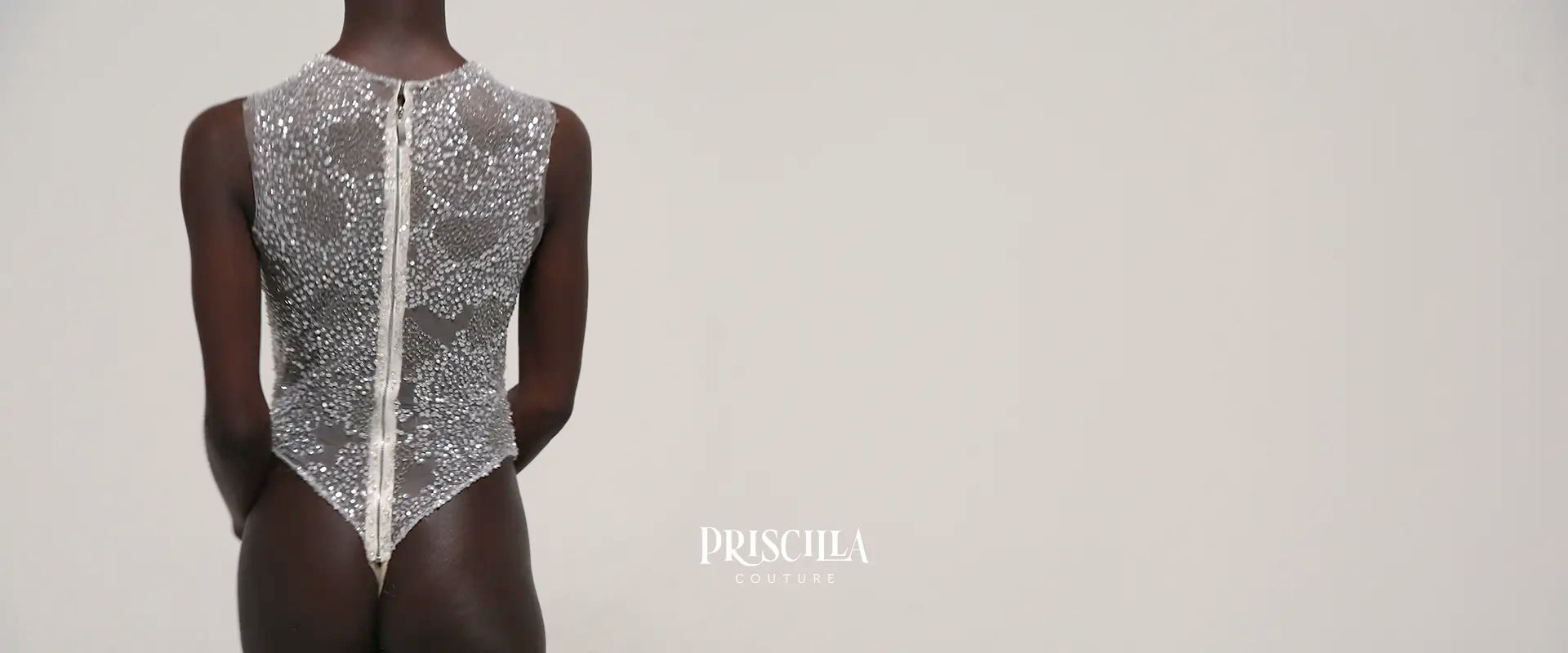 Rear view of a model in a sparkly Priscilla Couture beaded bodysuit with 'Priscilla Couture' branding on a light gray background