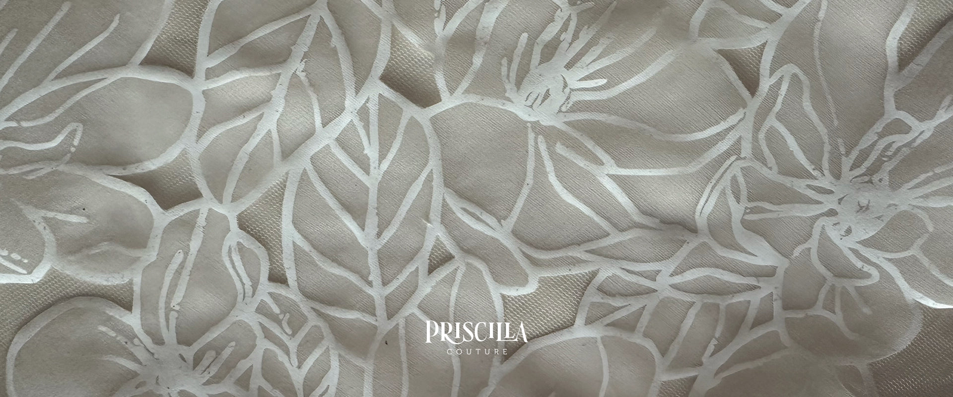 A close-up of a beige or taupe fabric with a raised, tonal floral pattern and the brand name 'PRISCILLA COUTURE' printed near the bottom center.