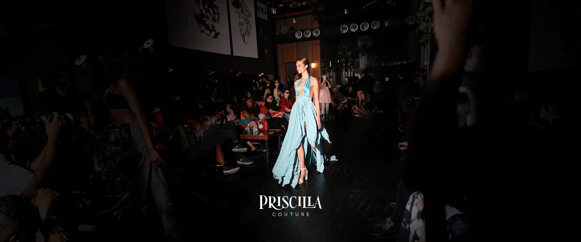 Model in a blue dress walking on a runway with 'Priscilla Couture' branding.